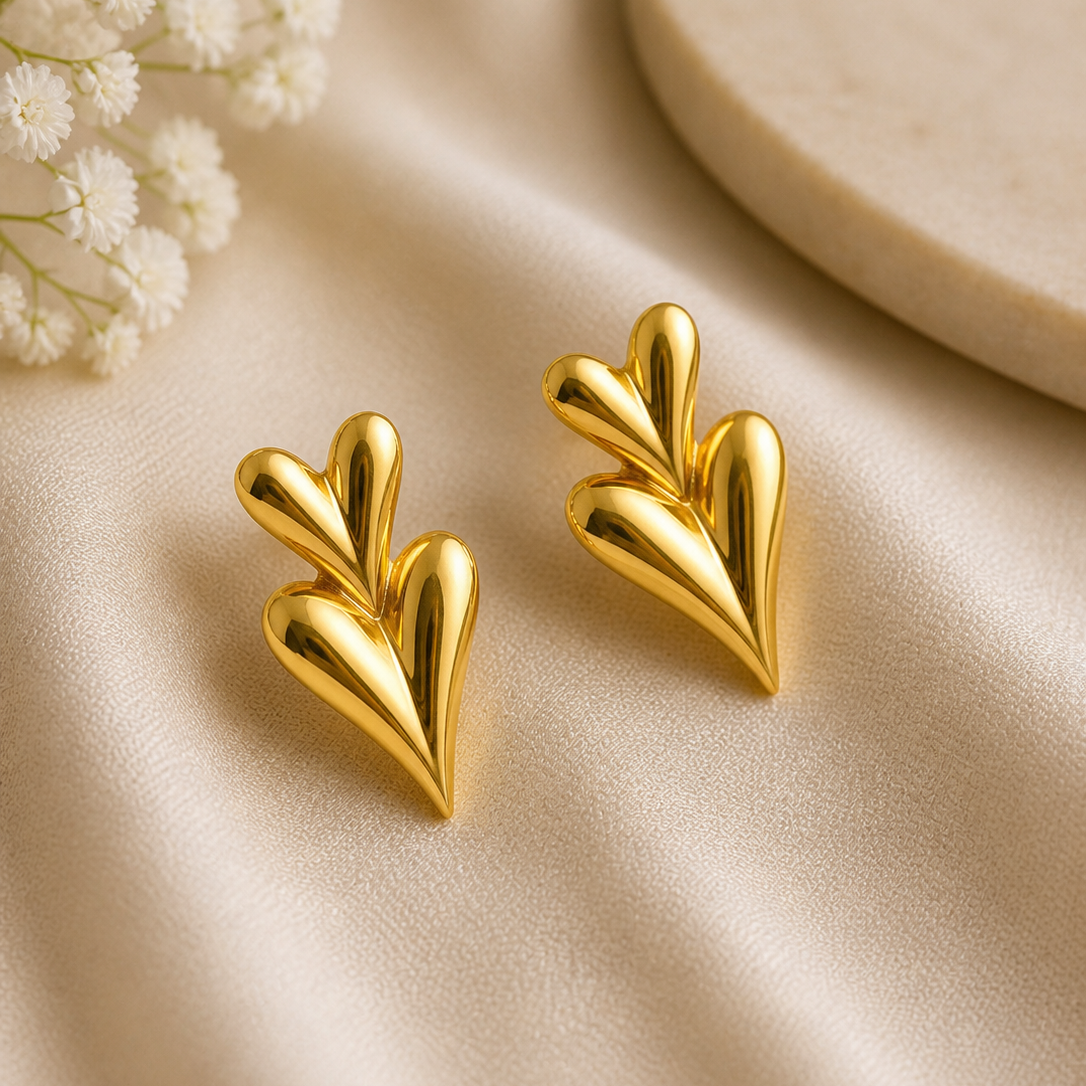 Gold leaf-shaped earrings on a beige fabric background with small white flowers.