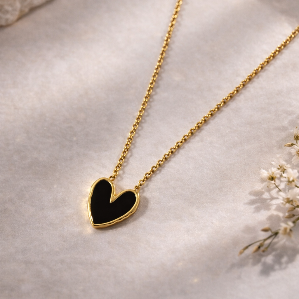 Gold necklace with a black heart pendant on a light background
