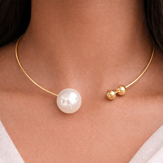 Gold necklace with a pearl pendant on a person wearing a white top.
