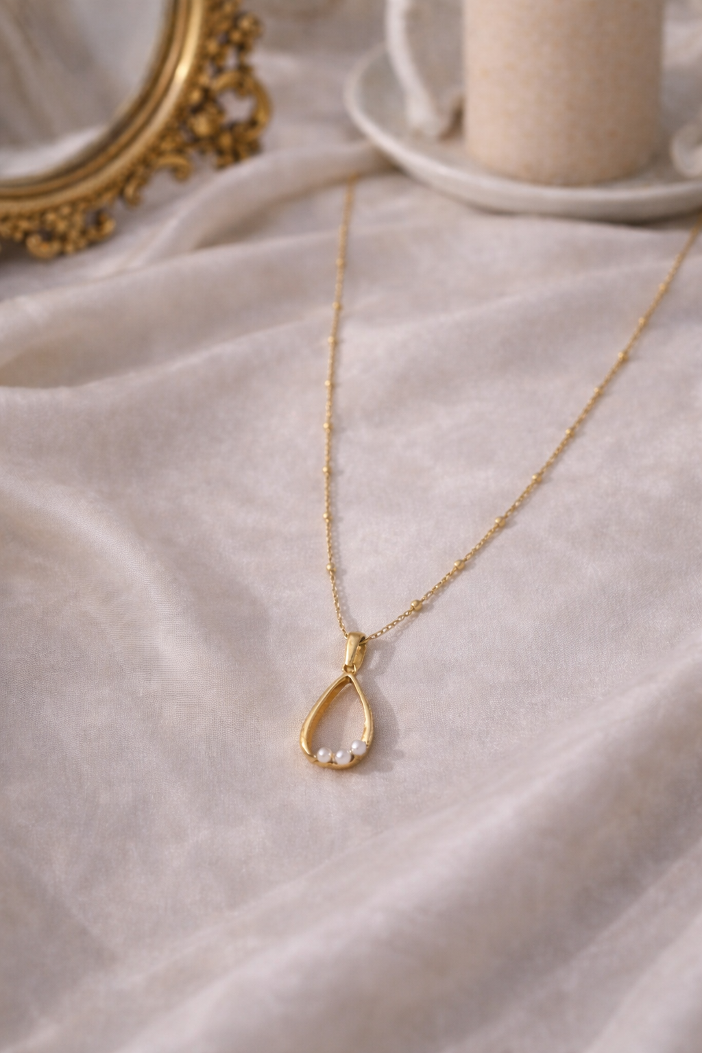 Gold necklace with a teardrop pendant on a soft fabric background