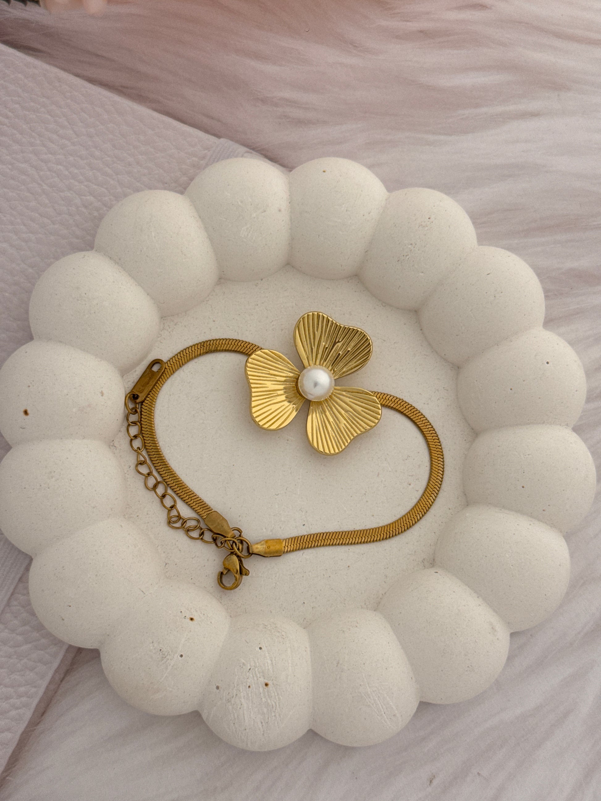 Gold bracelet with a pearl on a textured white surface