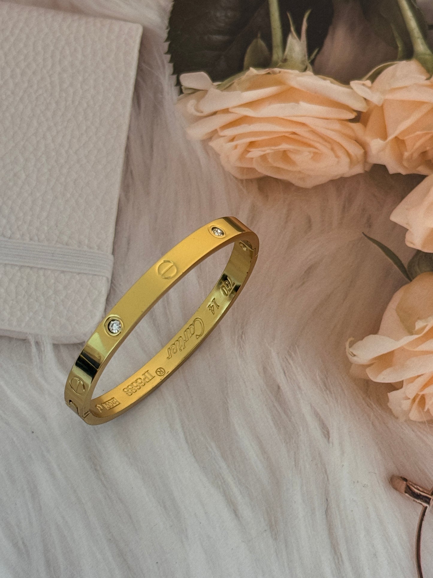 Gold bracelet with engraved text on a textured surface with flowers in the background