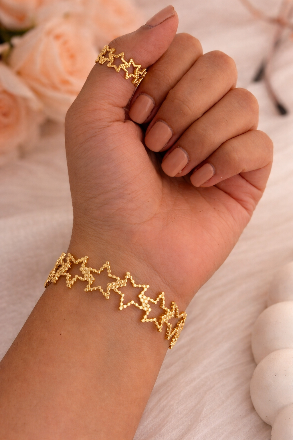 Gold star bracelet and ring on a hand with flowers in the background