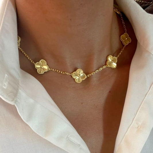 Gold necklace with clover-shaped pendants worn by a person in a white shirt.