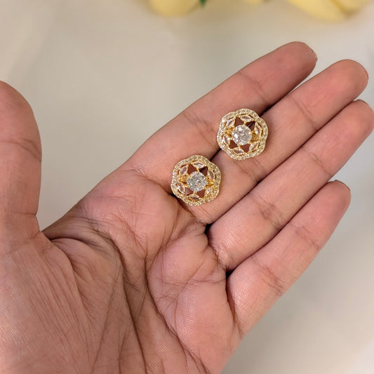 Gold earrings held in a hand with a blurred background