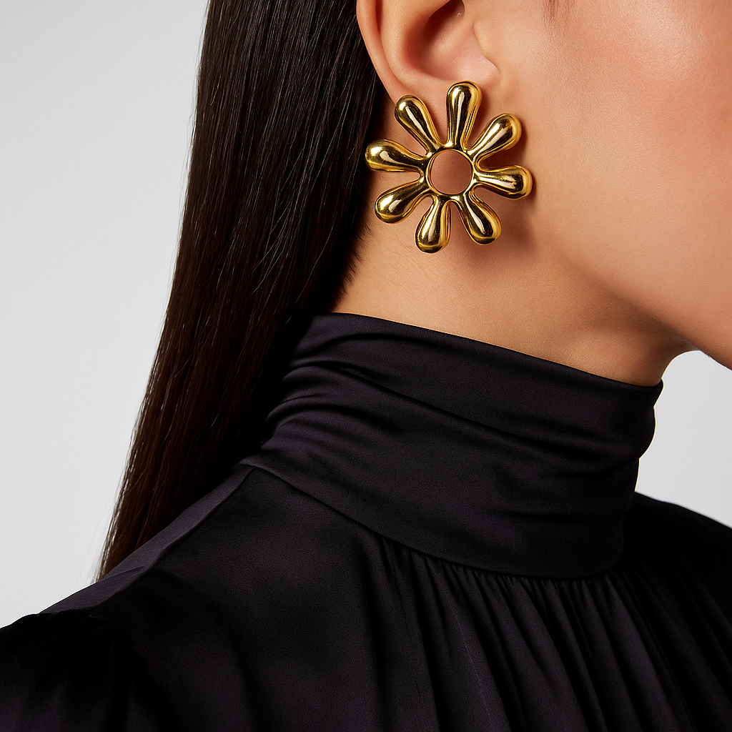 Gold flower-shaped earring worn by a person with a black top on a light gray background