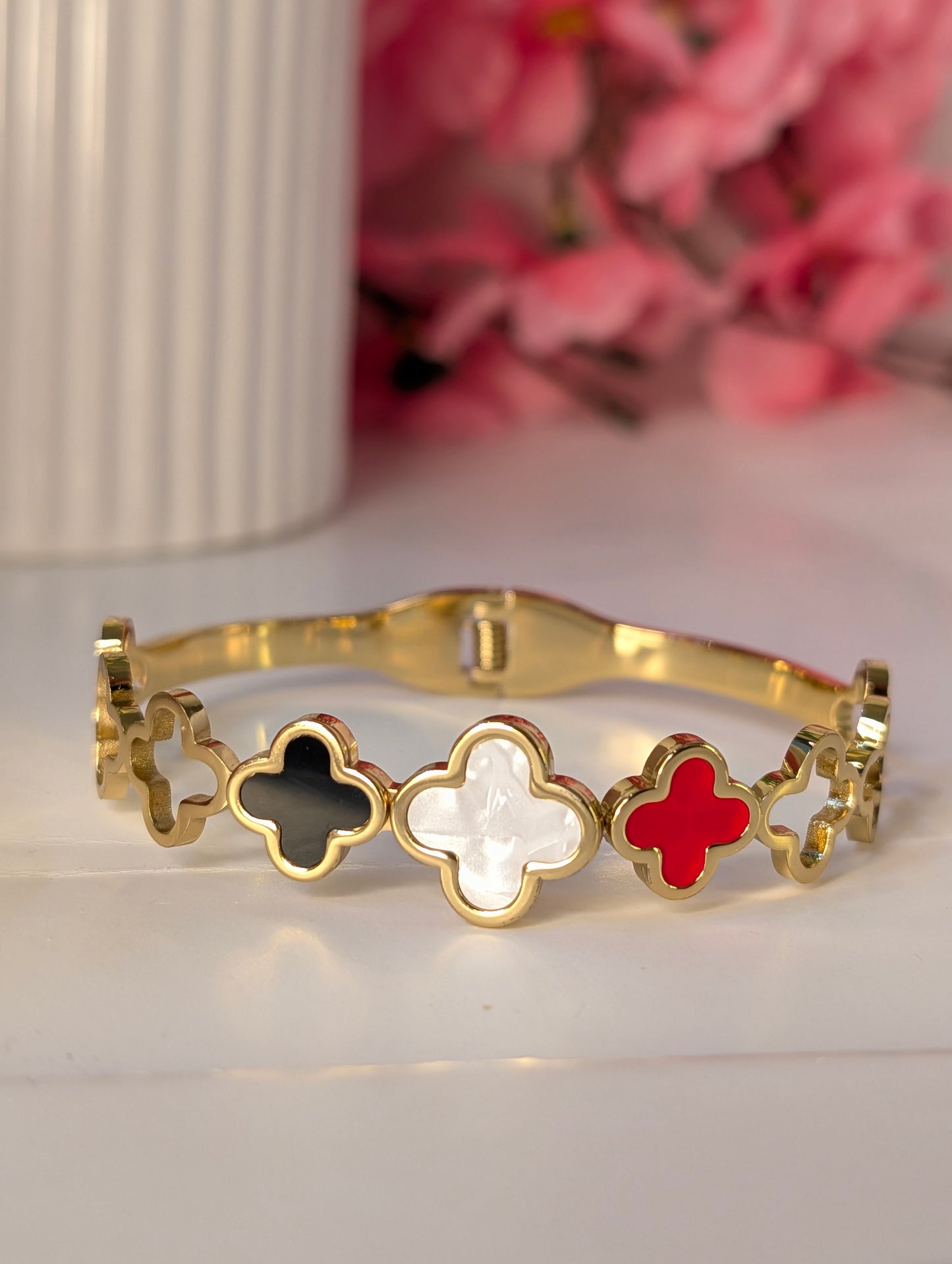 Gold bracelet with clover-shaped charms in black, white, and red on a light background.