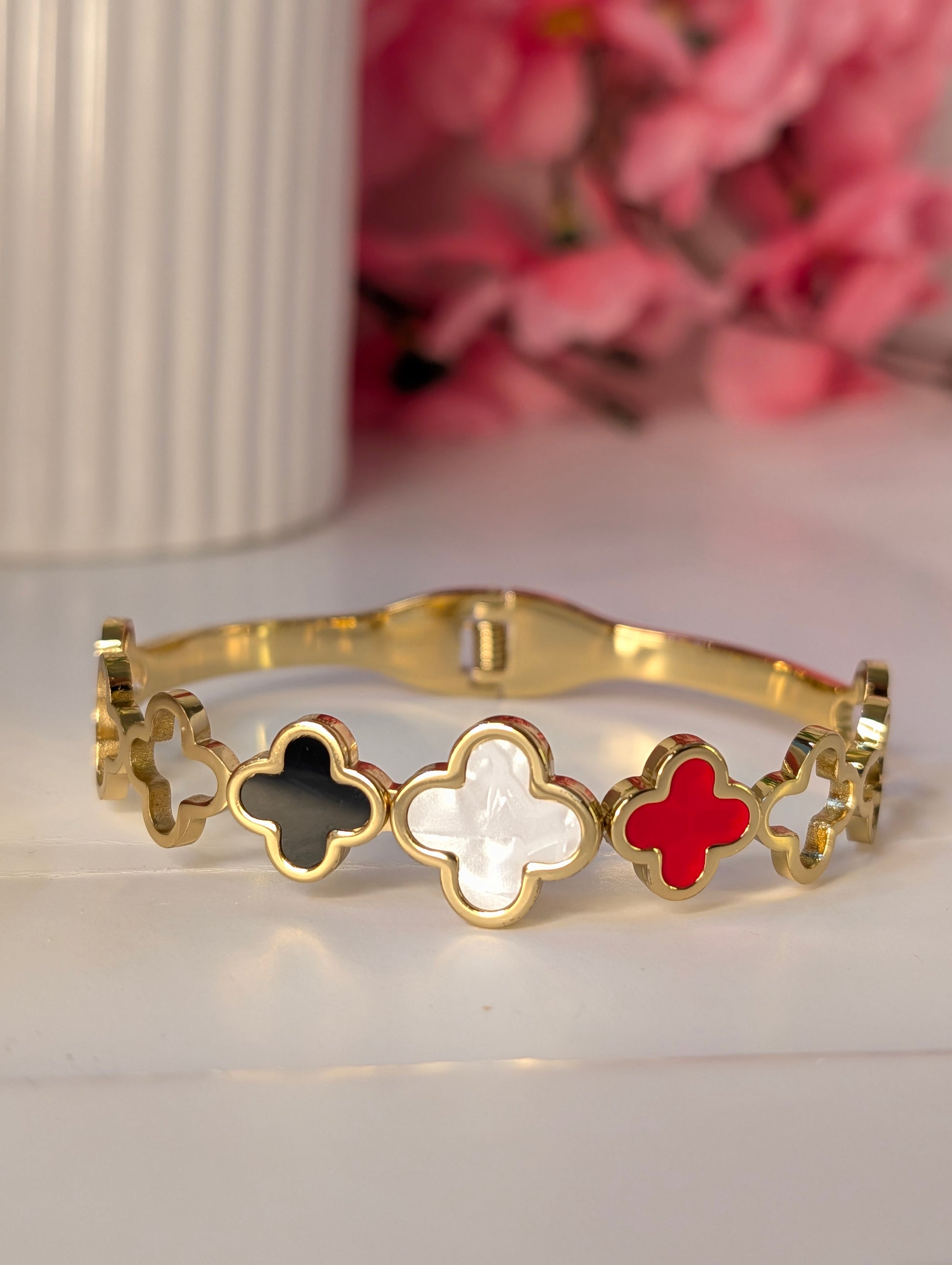 Gold bracelet with clover-shaped charms in black, white, and red on a light background.