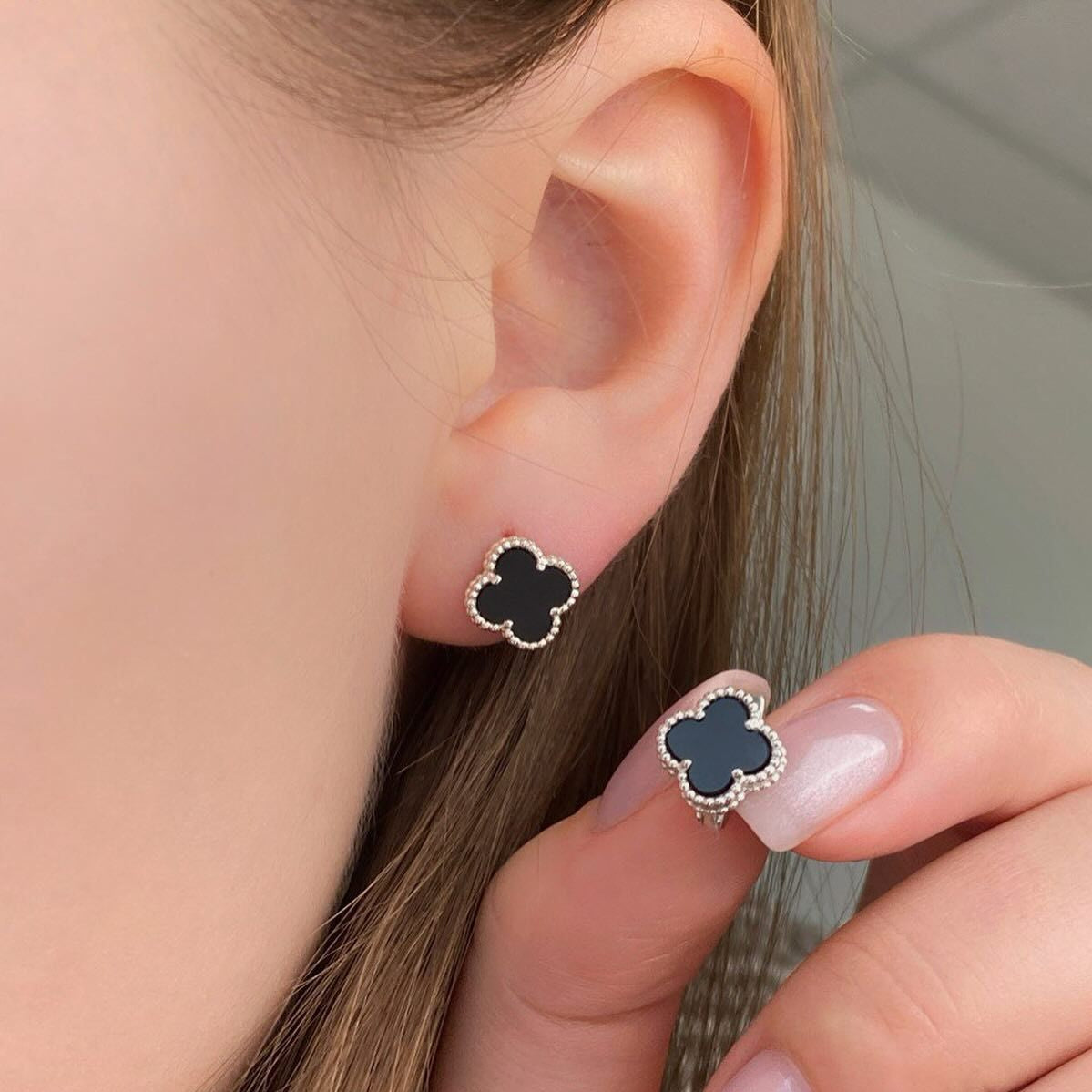 Close-up of a person wearing black clover-shaped earrings with a neutral background