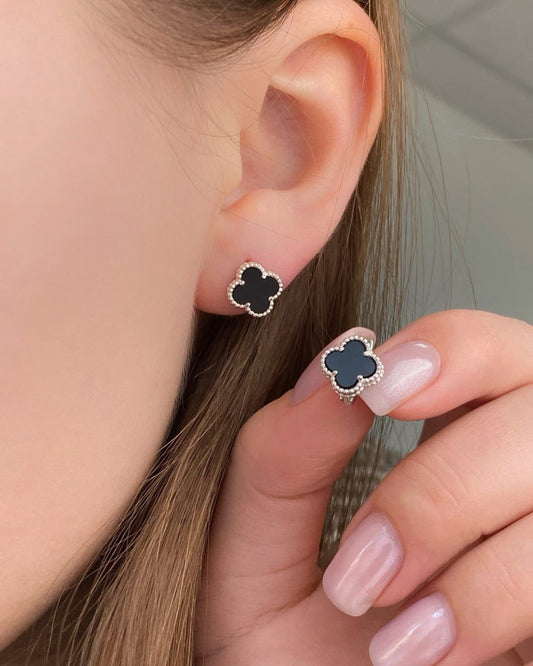 Close-up of a person wearing black clover-shaped earrings with a neutral background