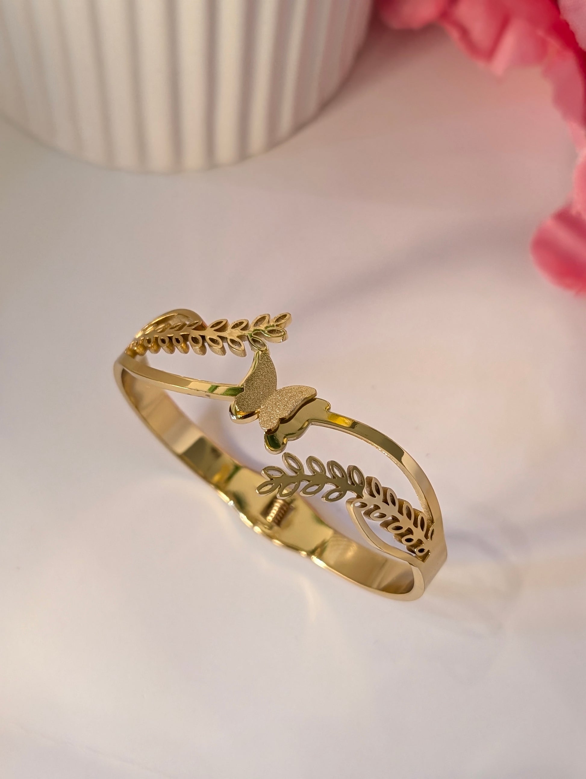 Gold bracelet with butterfly and leaf designs on a light background
