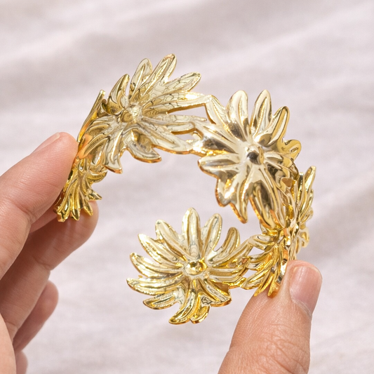 Gold floral headband held by a hand on a white fabric background