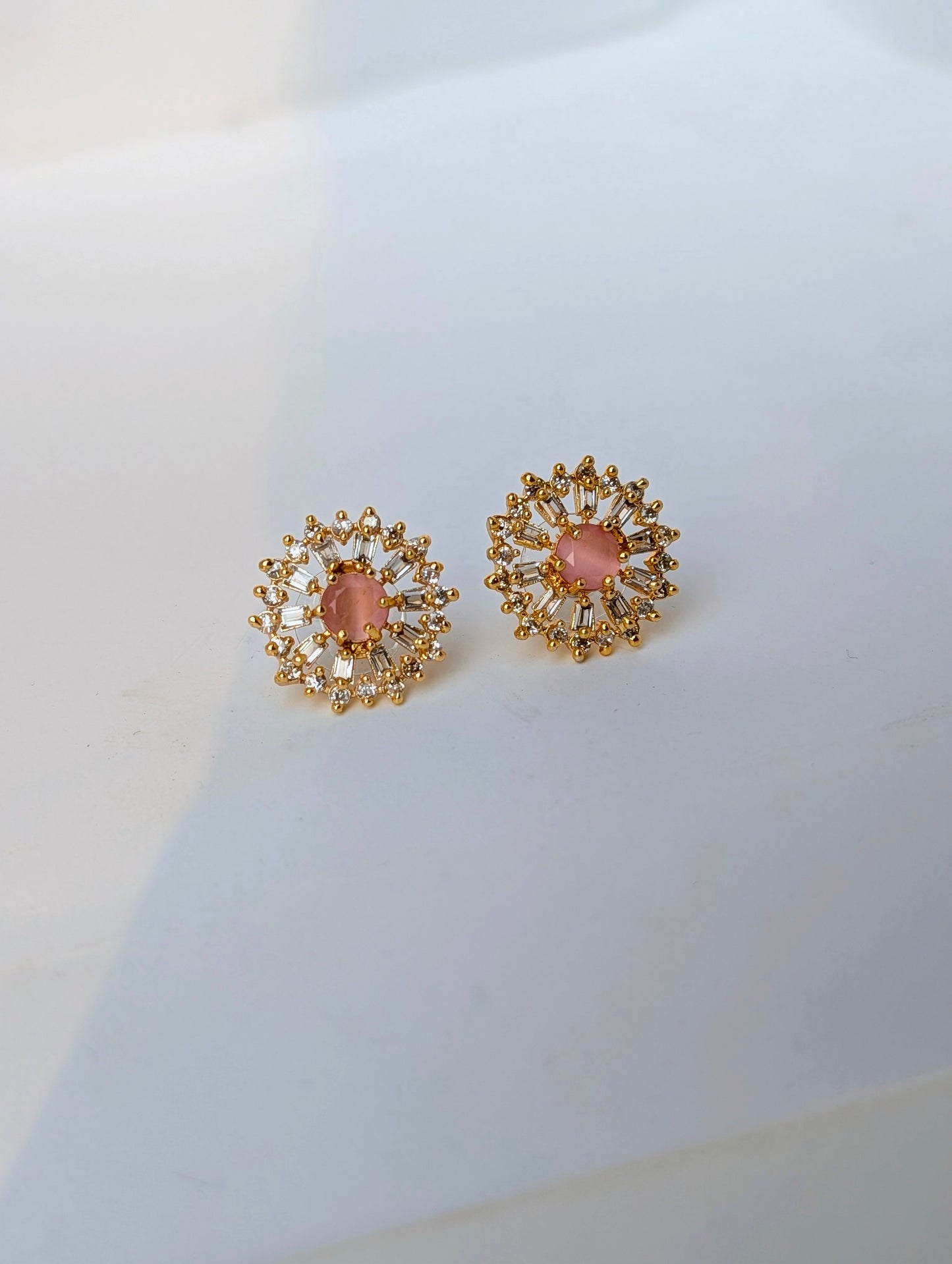 Gold earrings with pink gemstones on a light gray background
