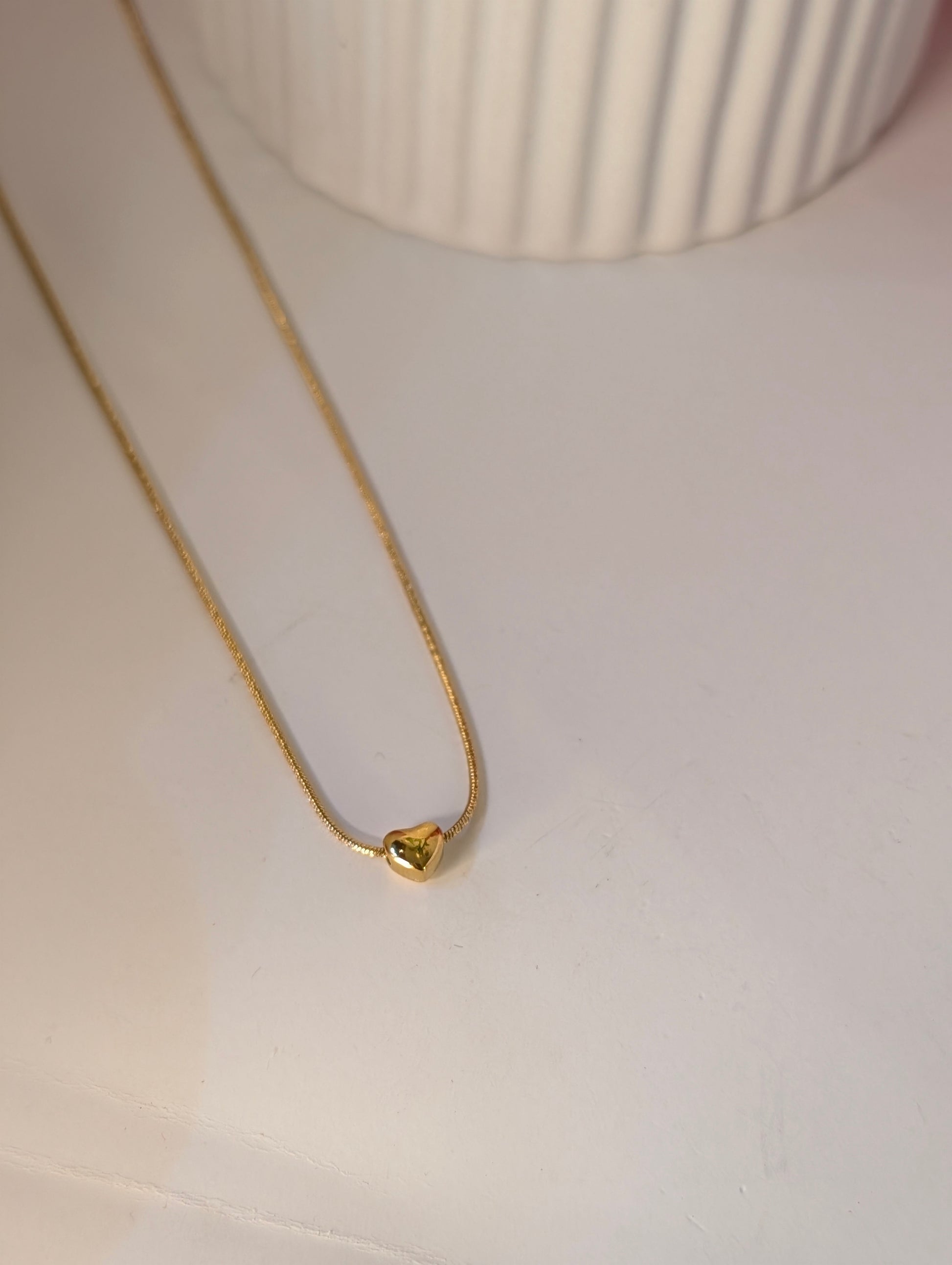 Gold necklace with a heart pendant on a light background