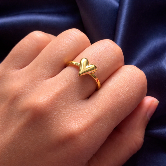 Gold heart-shaped ring on a hand with a dark blue satin background
