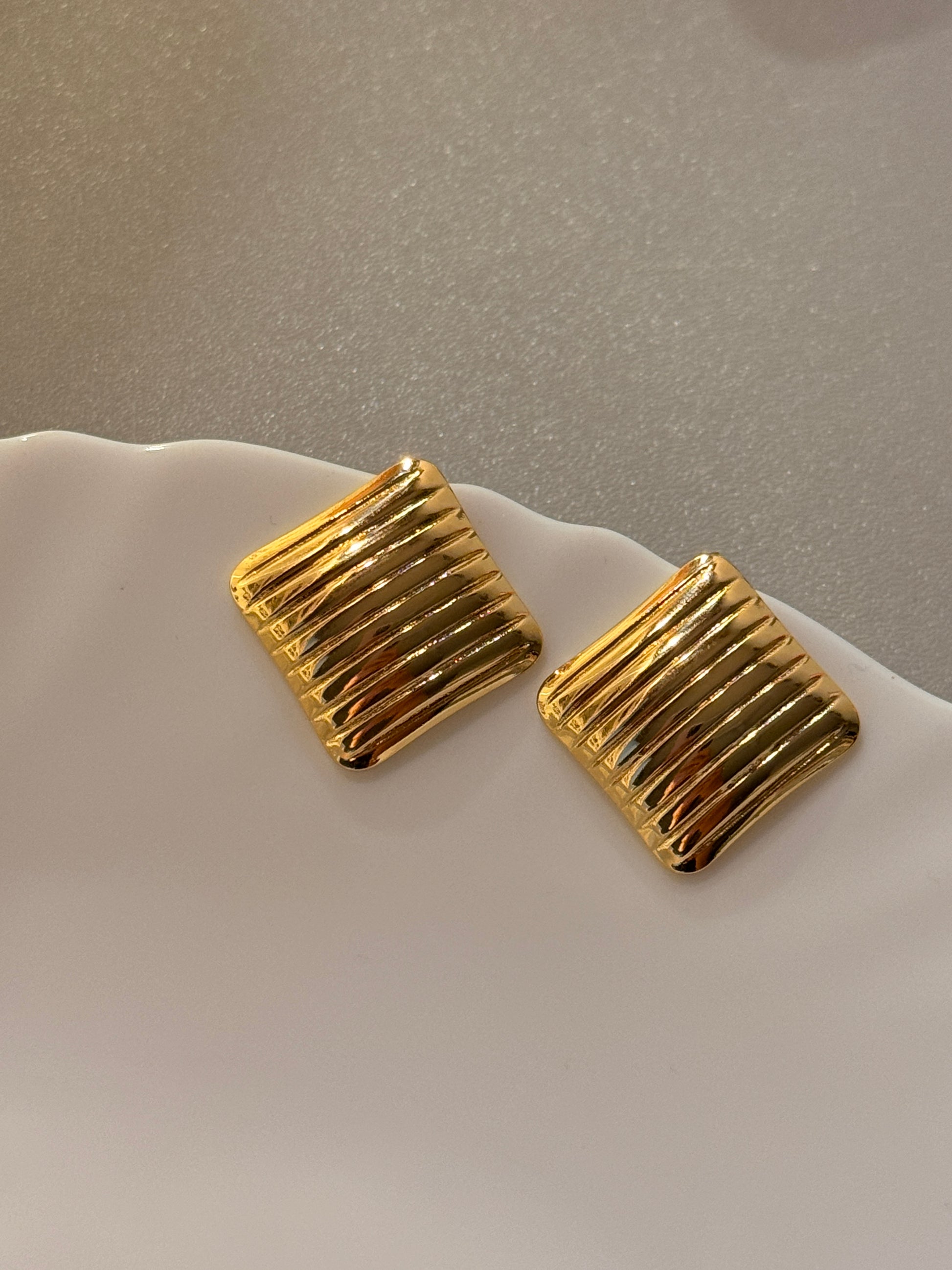 Gold square earrings on a light gray background