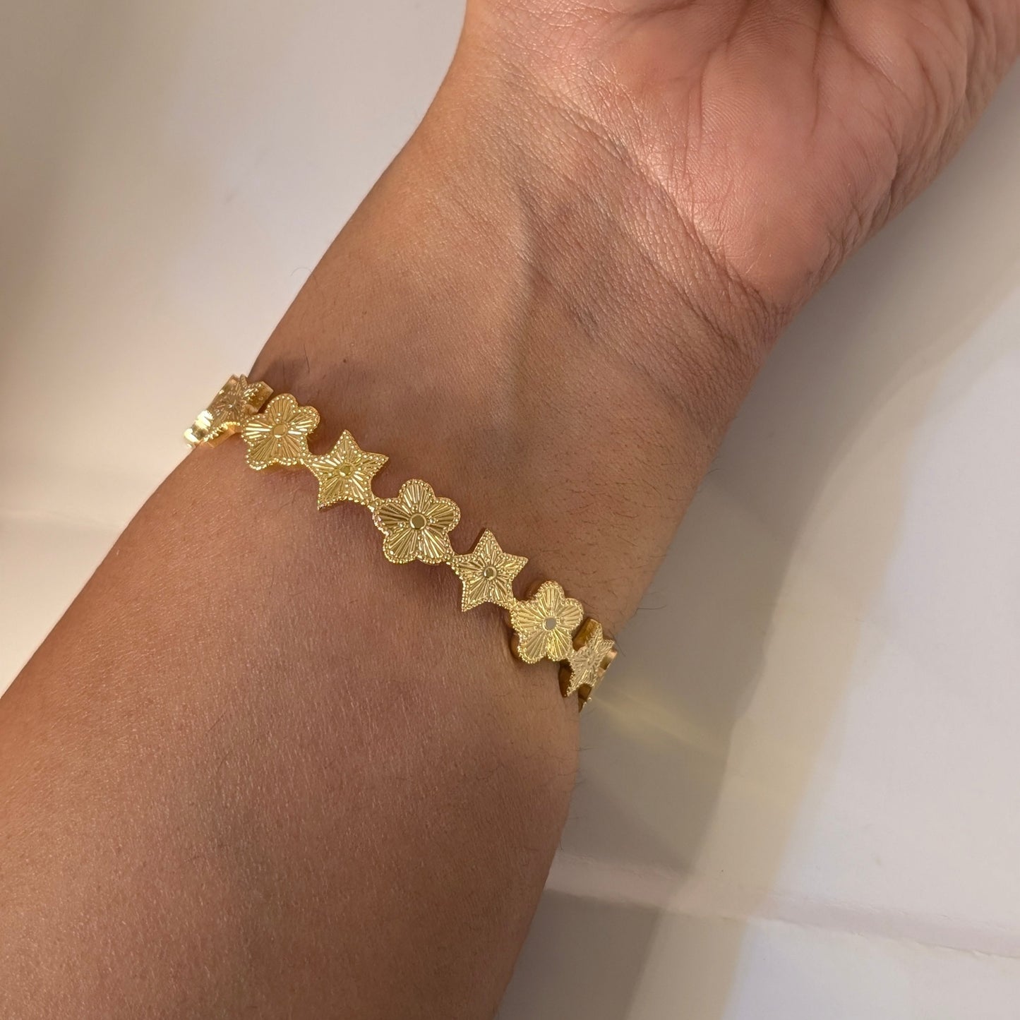 Gold bracelet with star designs on a wrist against a neutral background