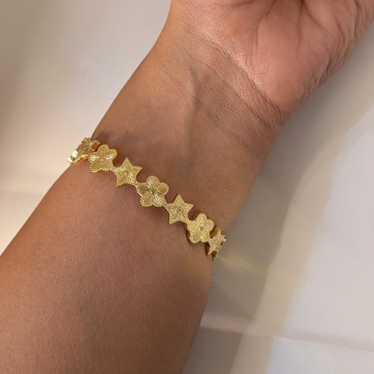 Gold bracelet with star designs on a wrist against a neutral background
