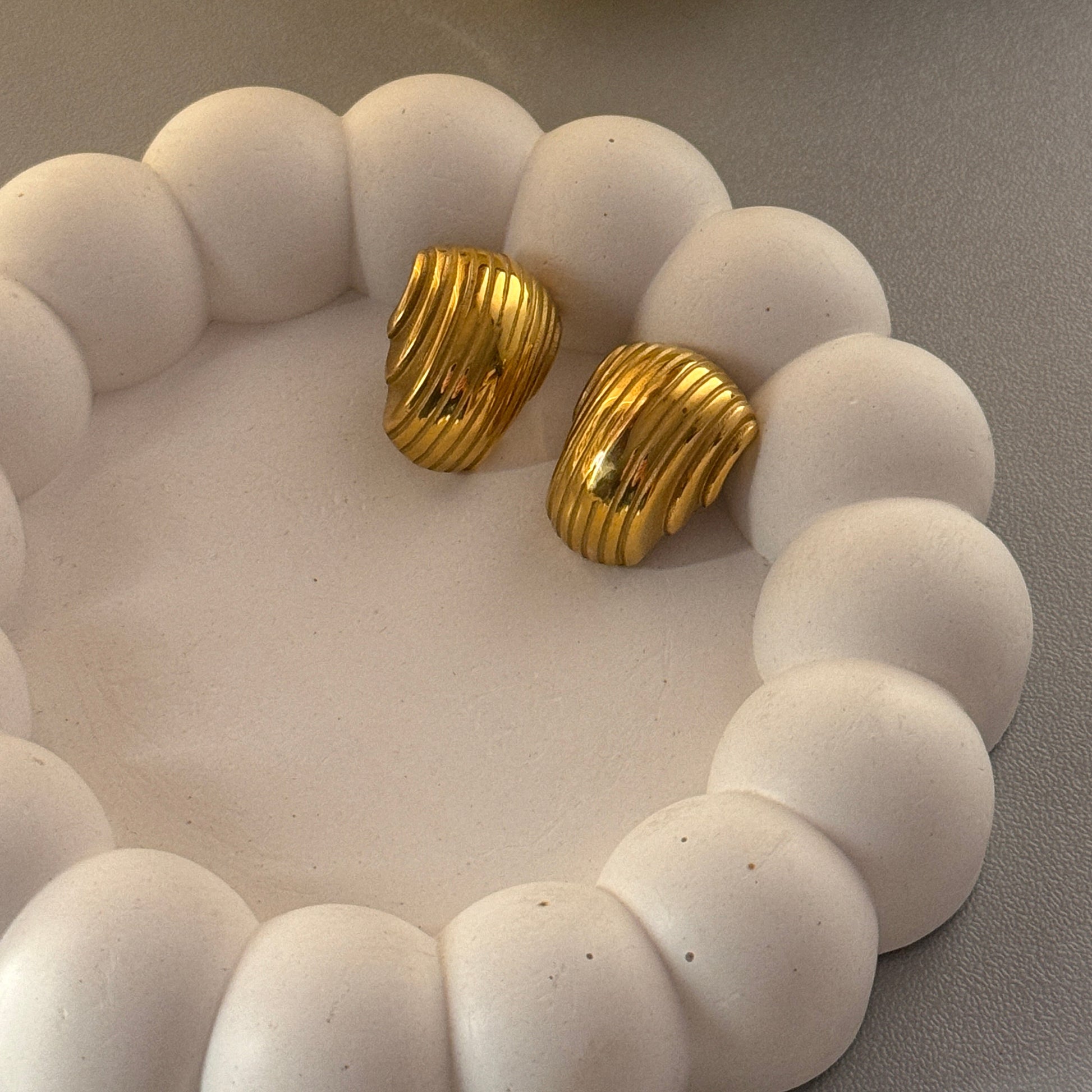 Gold earrings on a white textured surface with yellow tulips on the side.