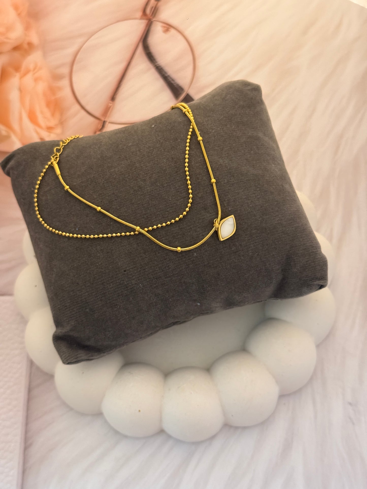 Gold necklace on a gray pillow with a soft white background