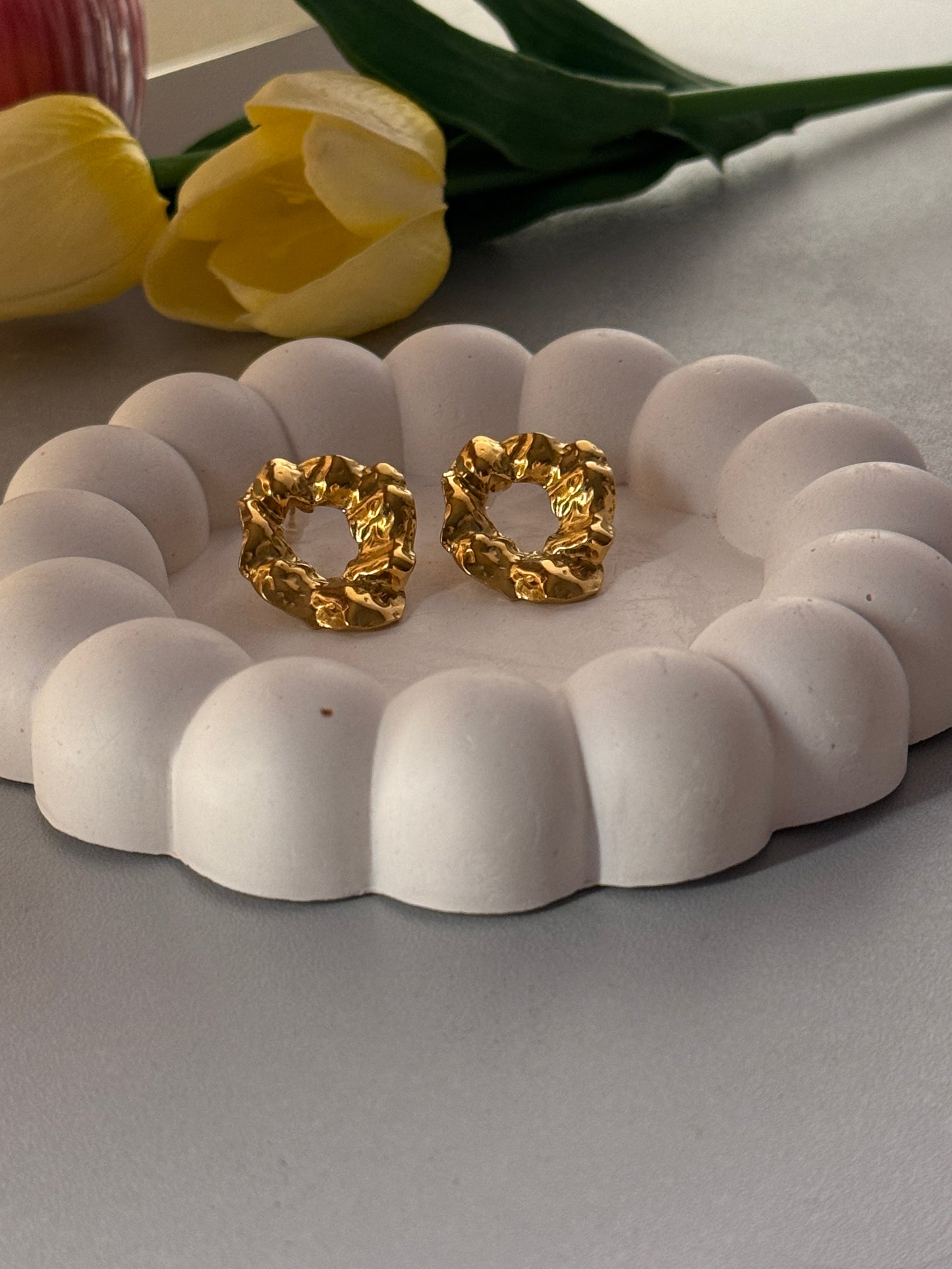 Gold earrings on a white decorative stand with yellow tulips in the background