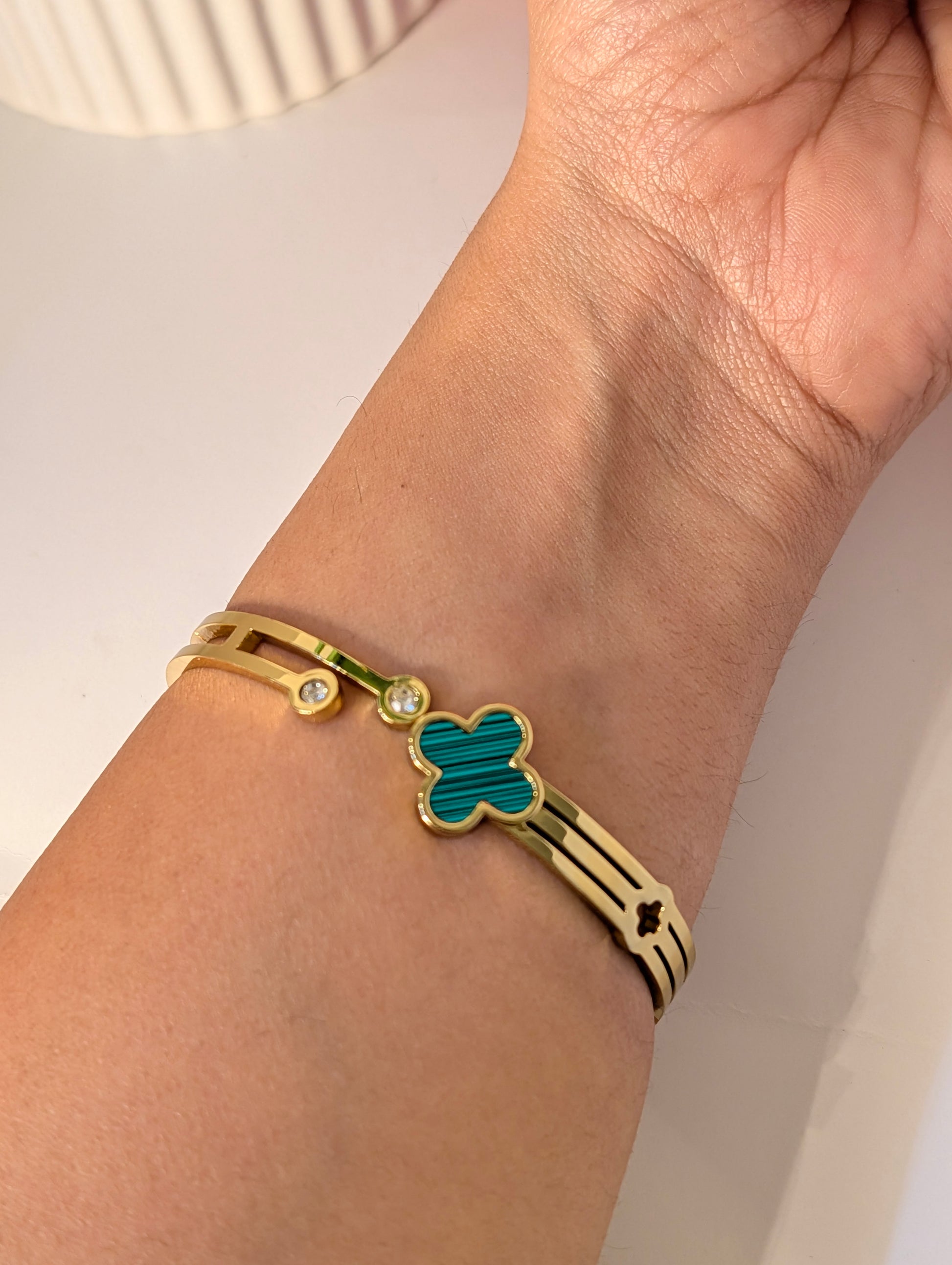 Gold bracelet with a green clover design on a wrist against a neutral background