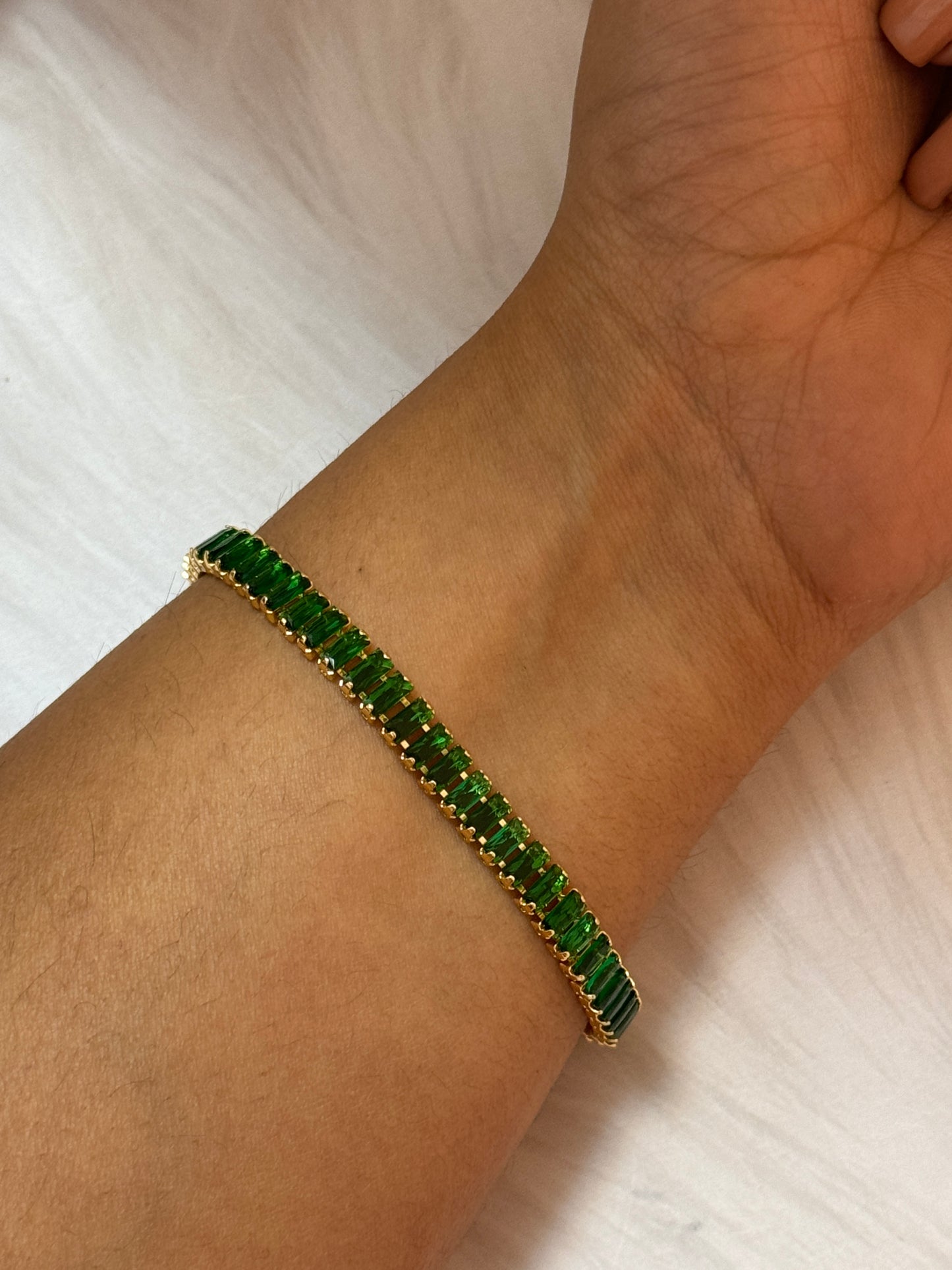 Green gemstone bracelet on a wrist against a light background