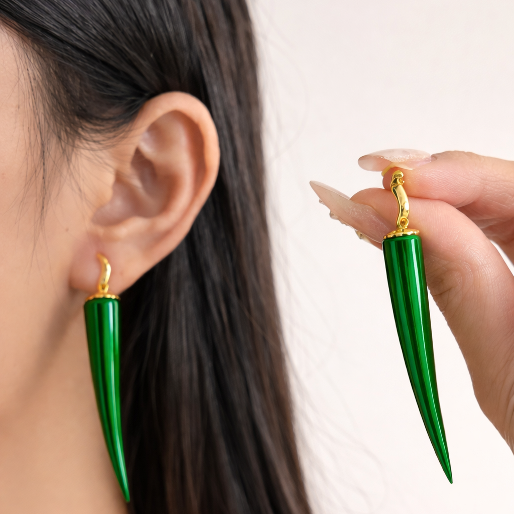 Green earrings with gold posts worn by a person against a neutral background