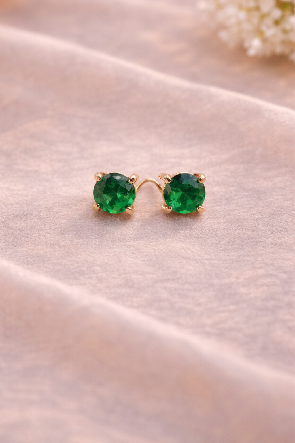 Pair of green gemstone earrings on a soft fabric background