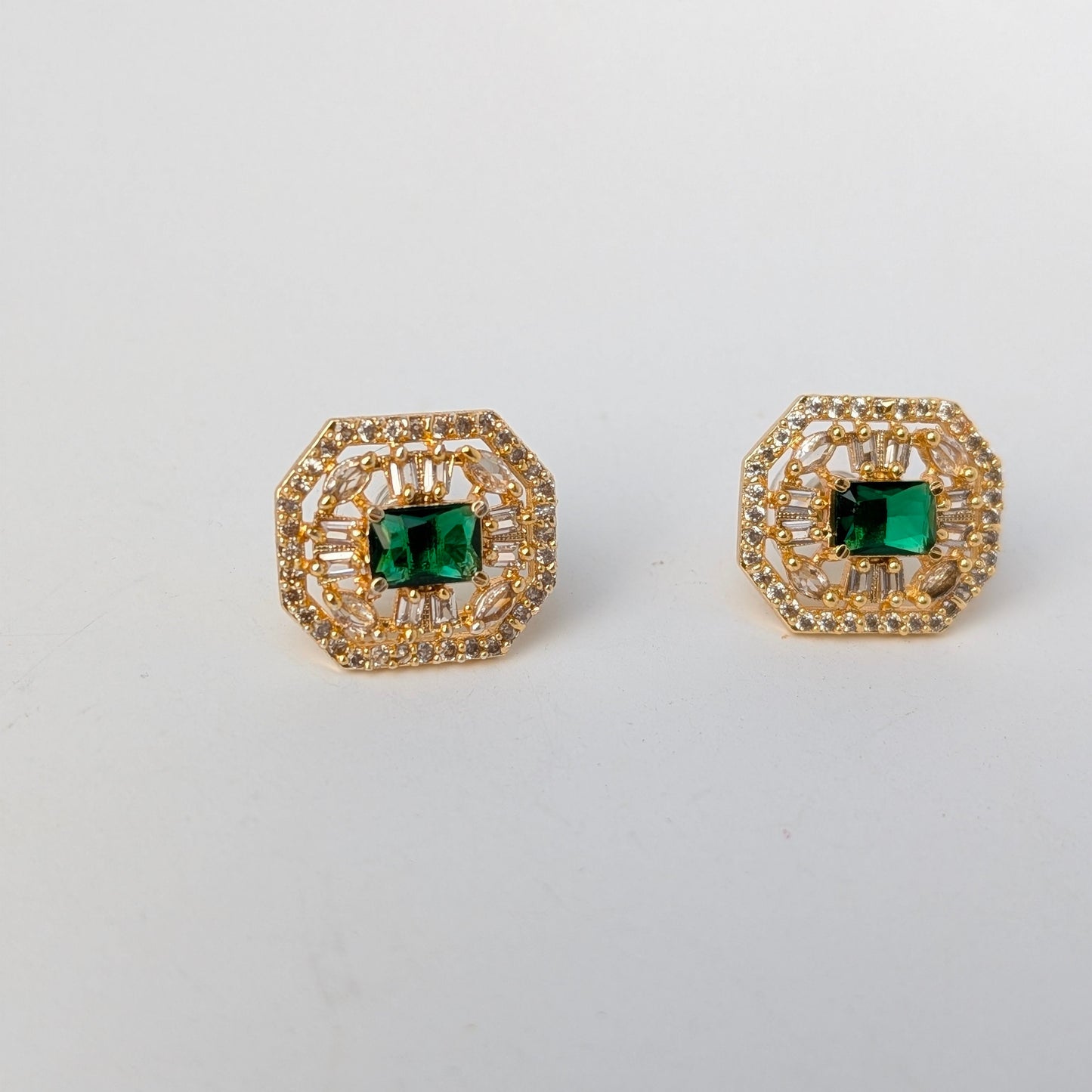 Gold earrings with green gemstones on a light gray background