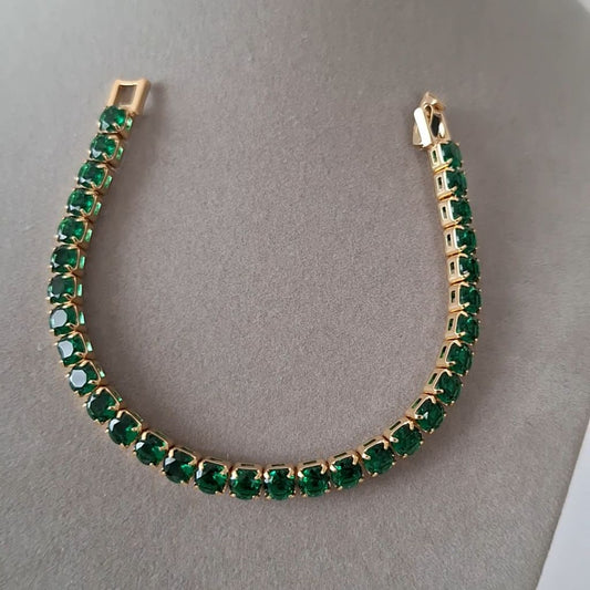 Gold bracelet with green gemstones on a gray background