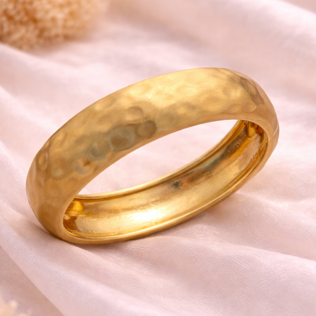 Gold ring with a textured surface on a soft pink fabric background