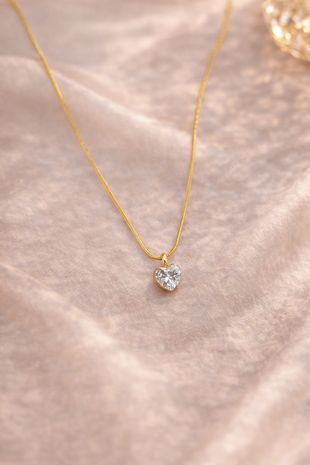 Gold necklace with a heart-shaped pendant on a soft pink fabric background