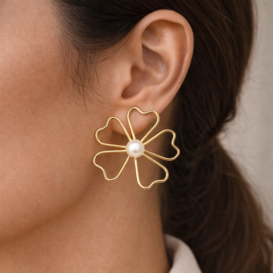 Gold flower-shaped earring with a pearl center worn by a person.