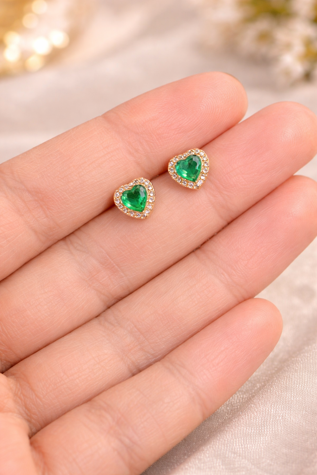 Heart-shaped emerald earrings on a hand with a blurred background