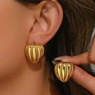 Gold heart-shaped earrings worn by a person with blurred background