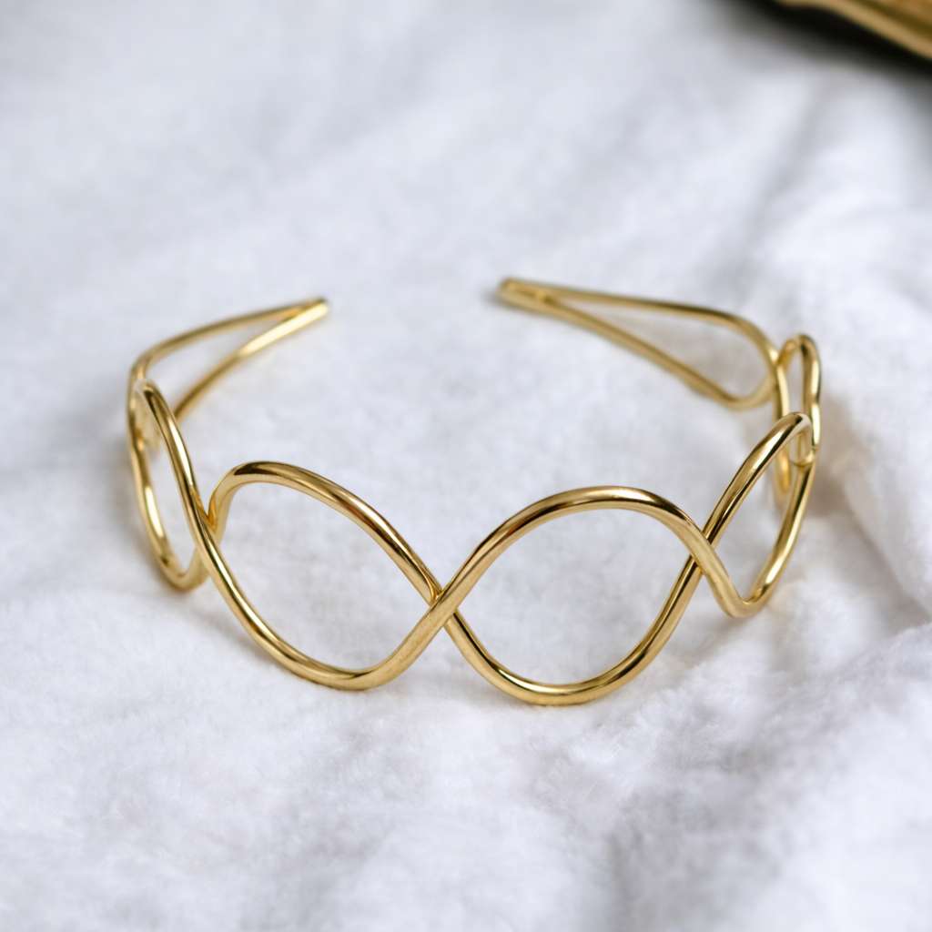 Gold bracelet with a wavy design on a white fabric background