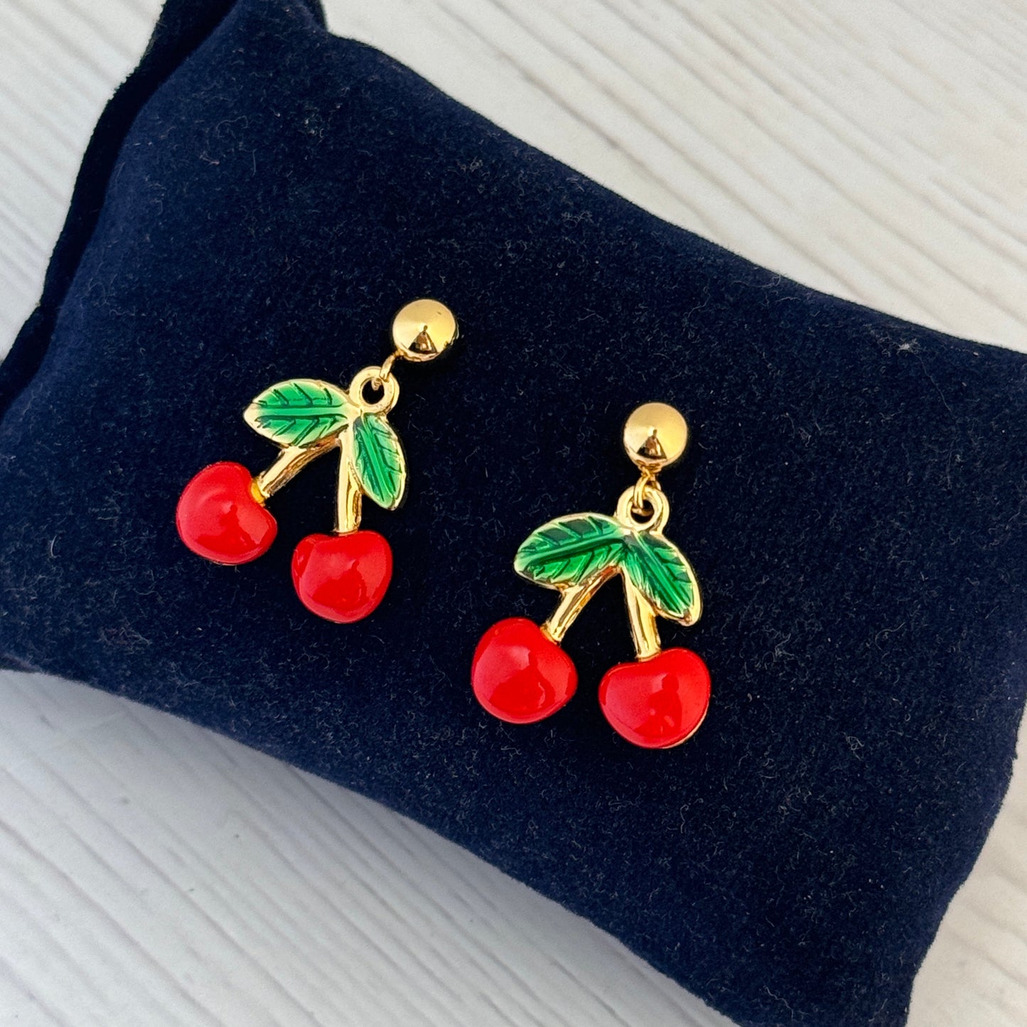 Cherry-themed earrings on a dark blue velvet cushion.
