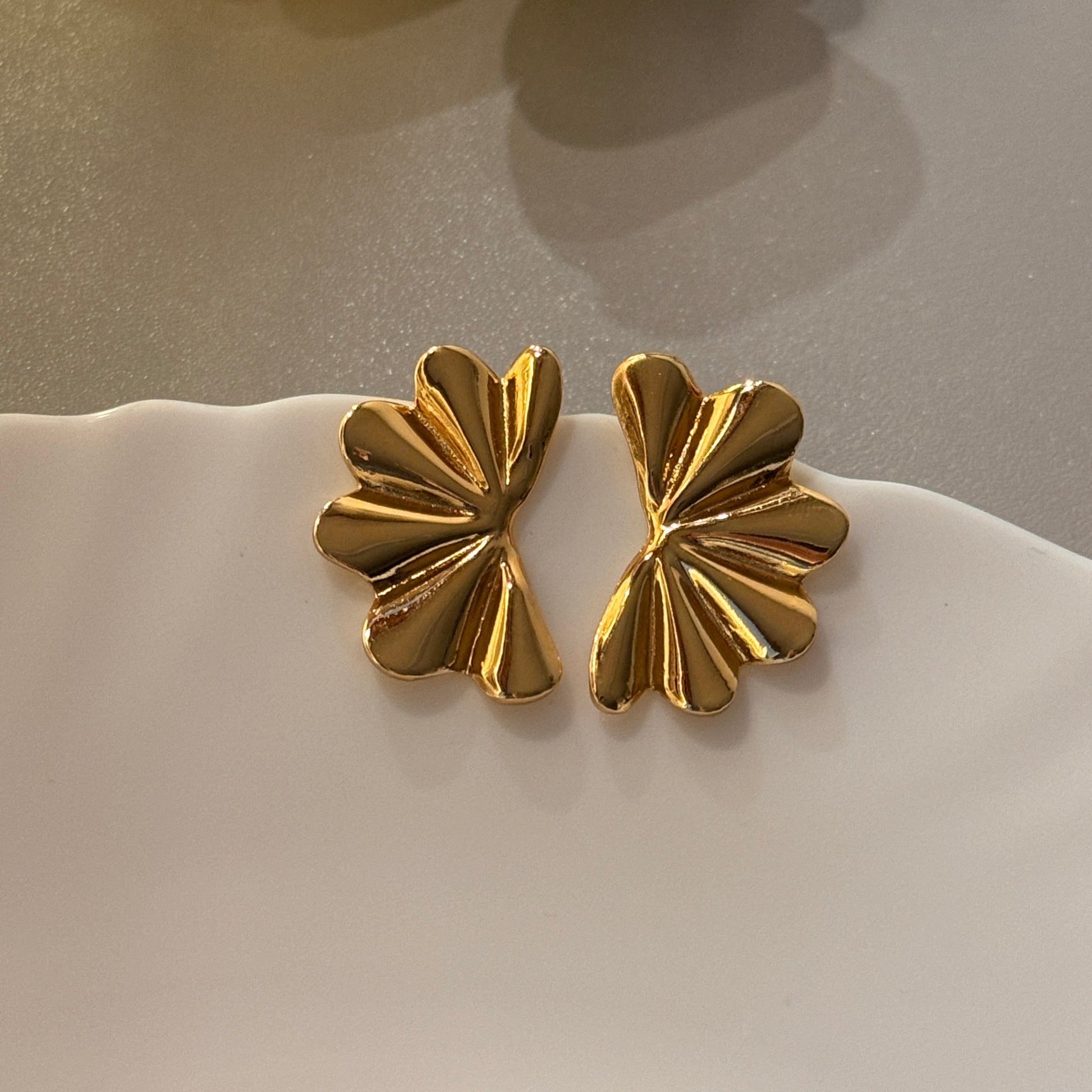 Pair of gold butterfly-shaped earrings on a white stand.