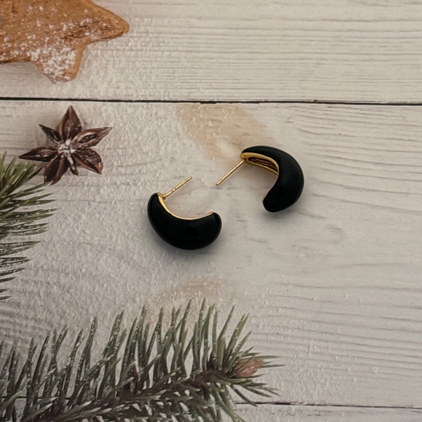 Black and gold earrings on a wooden surface with a star-shaped cookie and pine branch.