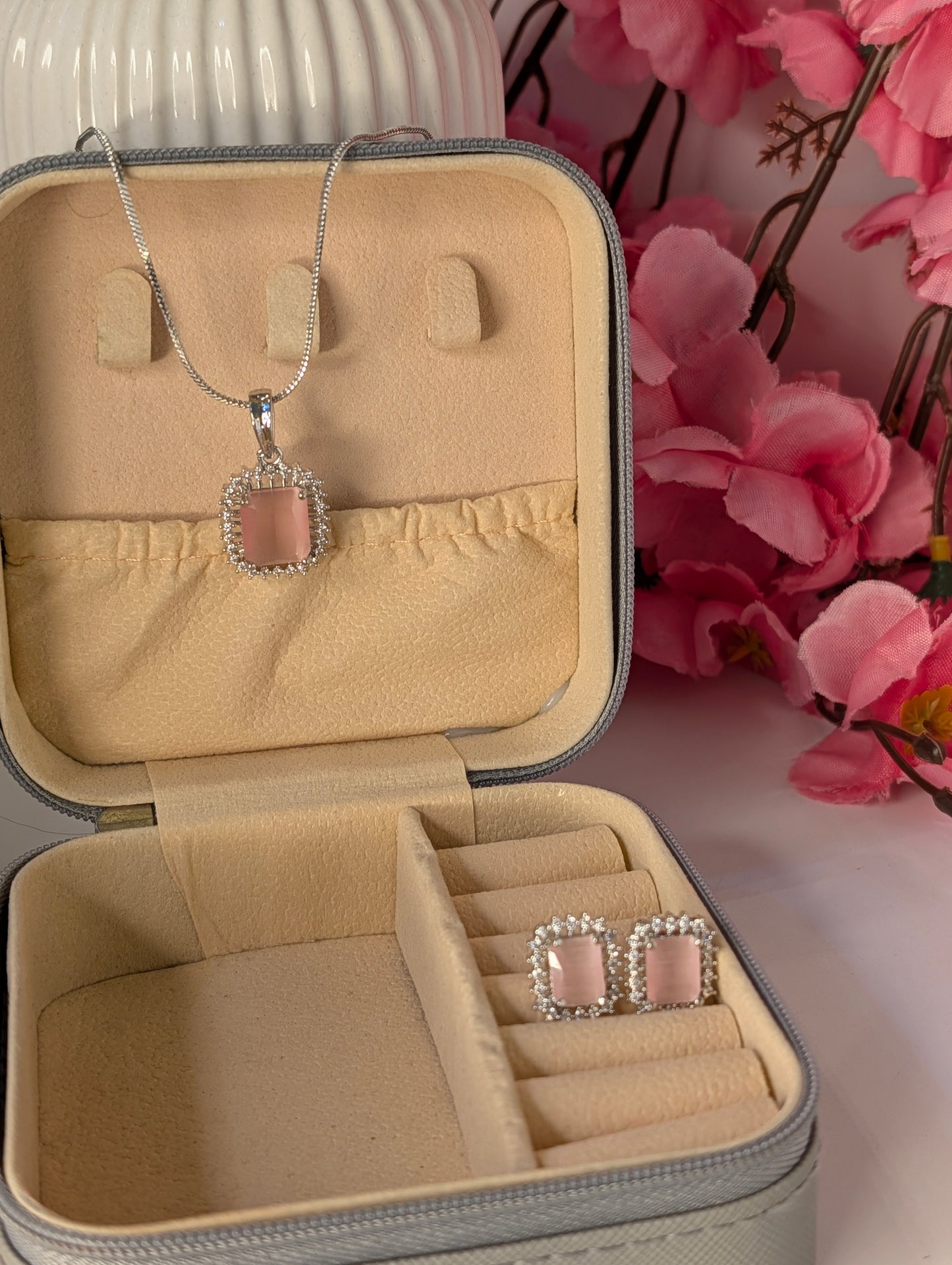Jewelry set with necklace and earrings in a beige jewelry box with pink flowers in the background