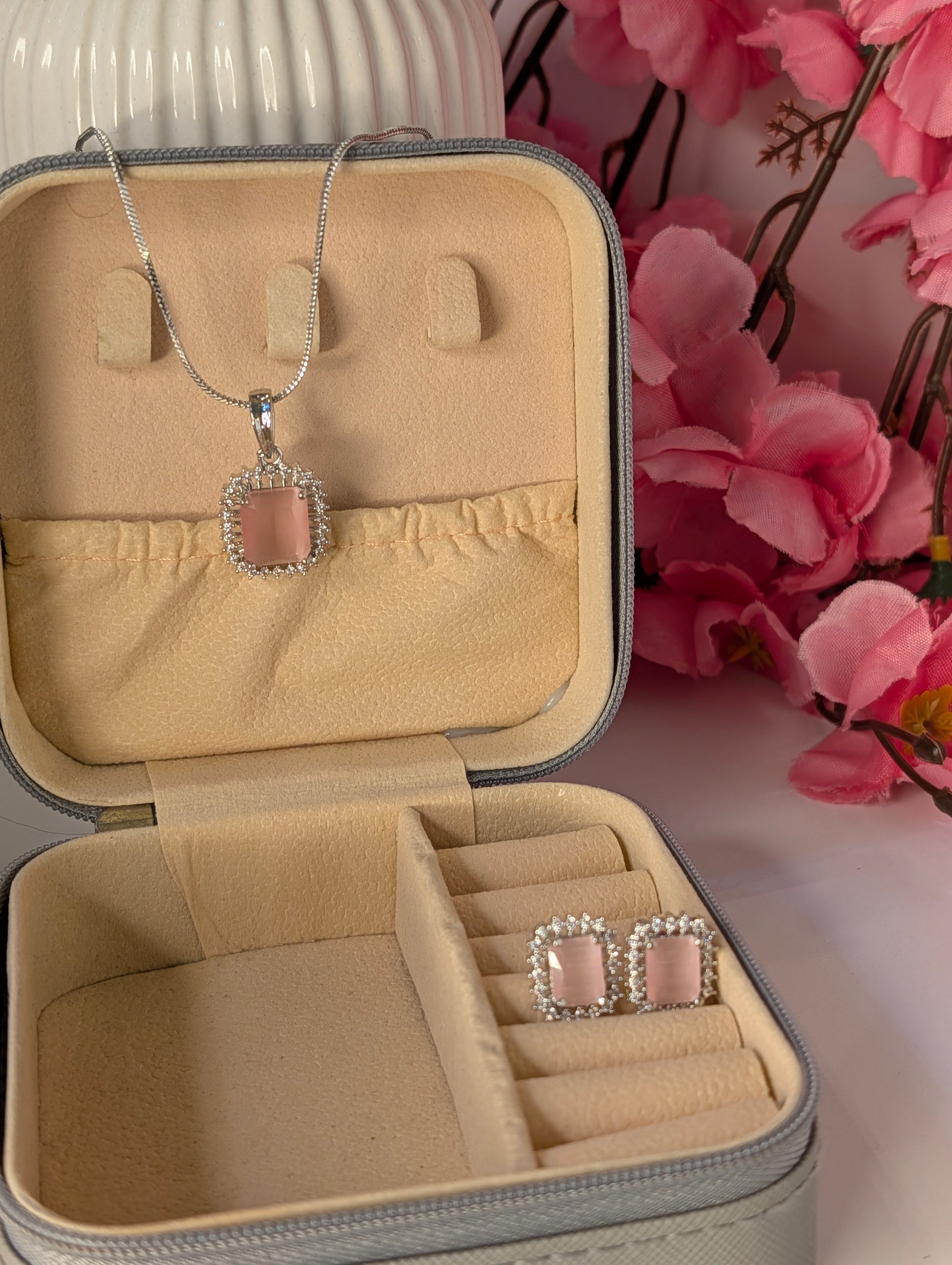 Jewelry set with necklace and earrings in a beige jewelry box with pink flowers in the background