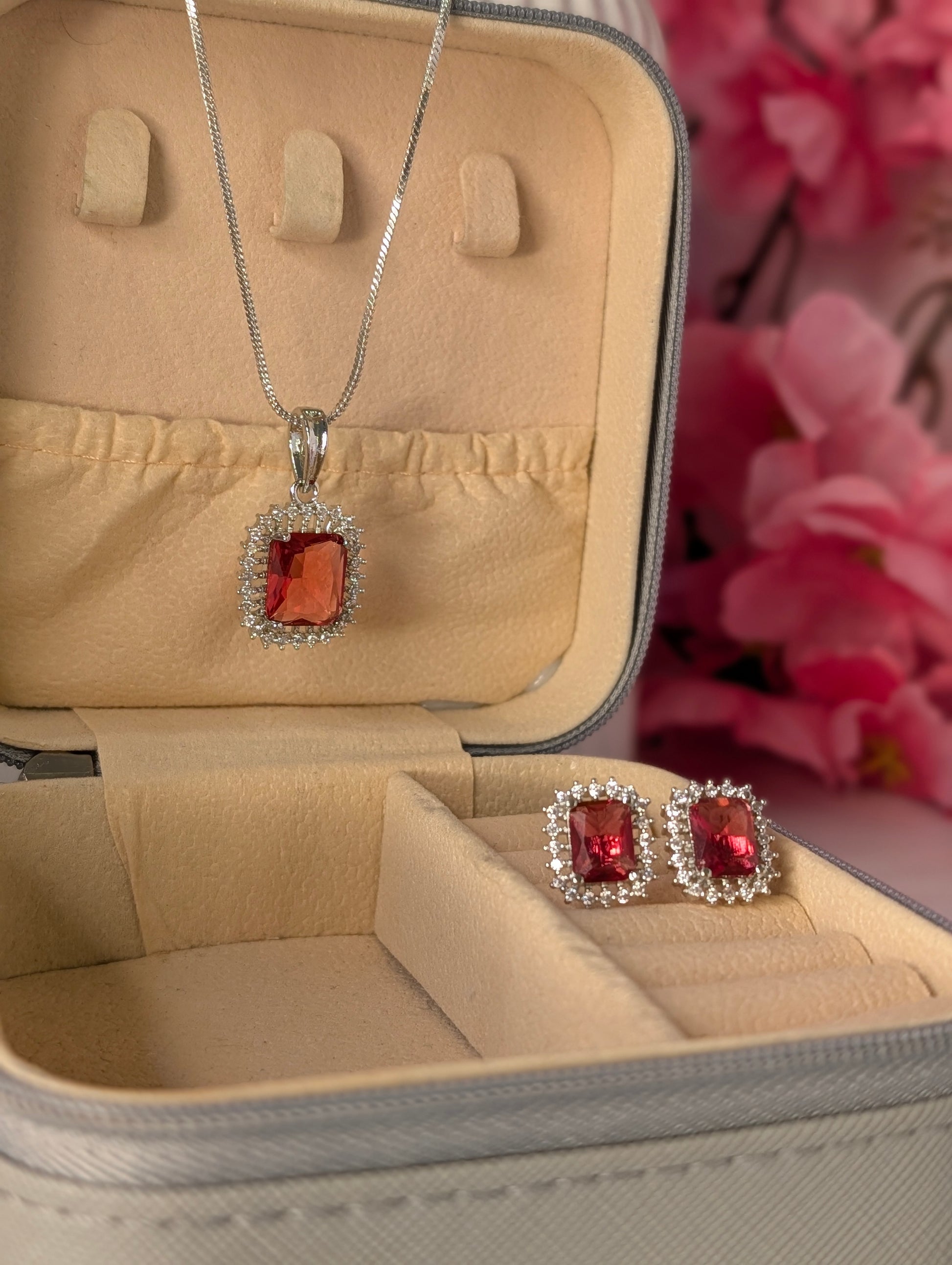 Jewelry set with pendant and earrings in a beige jewelry box with pink flowers in the background.