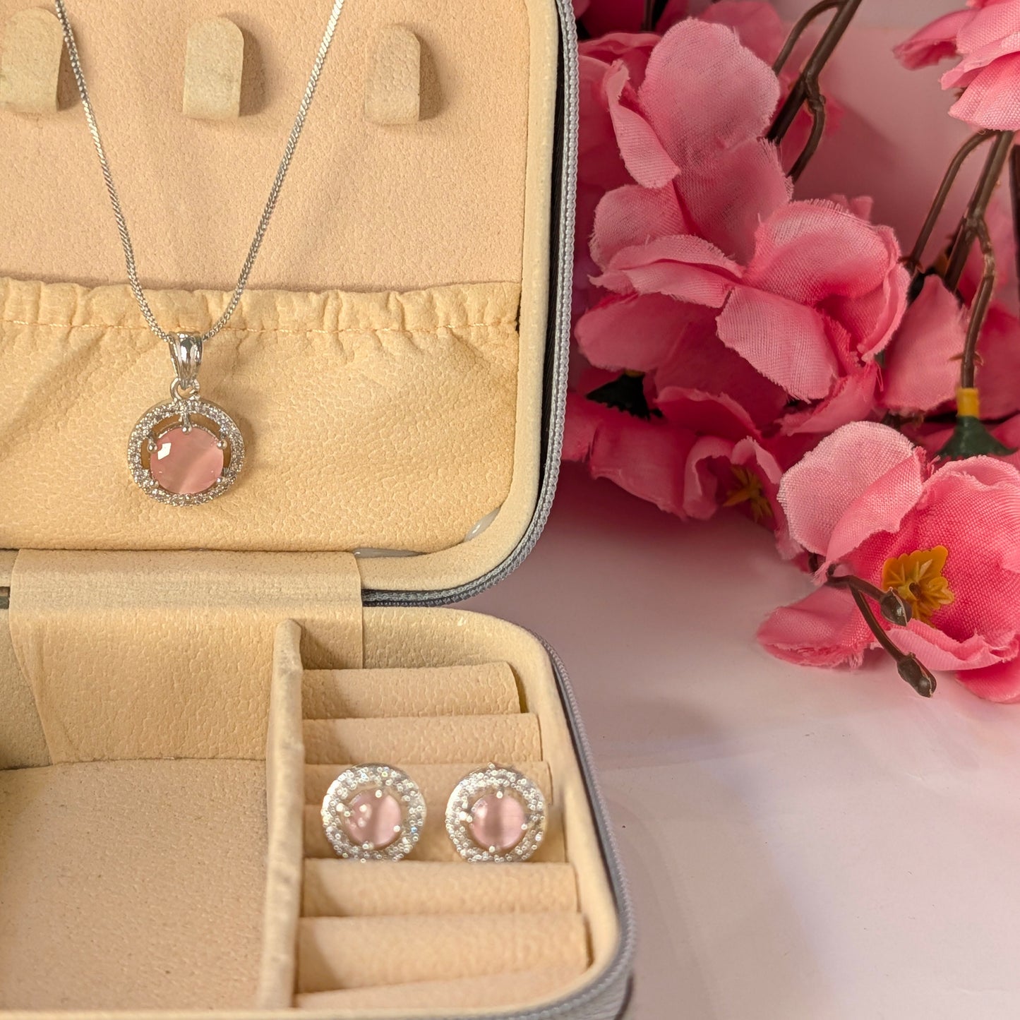 Jewelry set with pink stones in an open jewelry box, surrounded by pink flowers.
