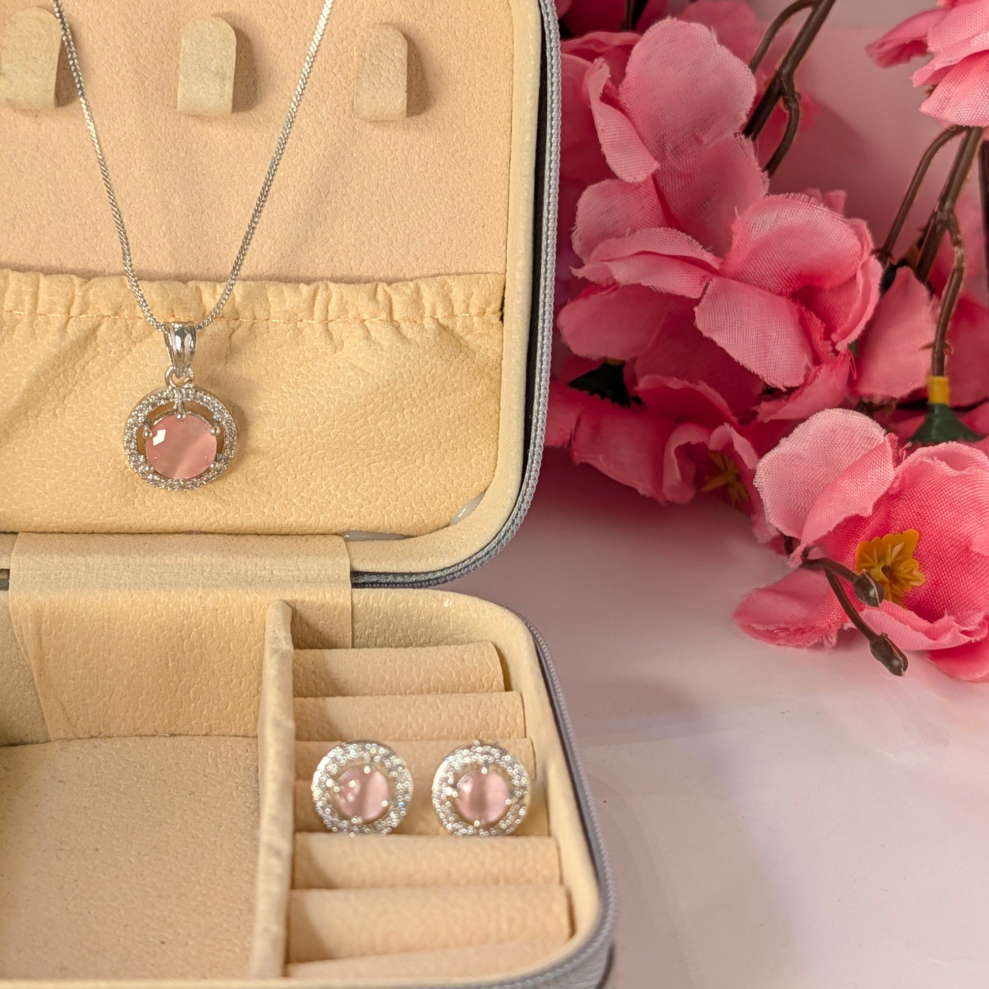 Jewelry set with pink stones in an open jewelry box, surrounded by pink flowers.
