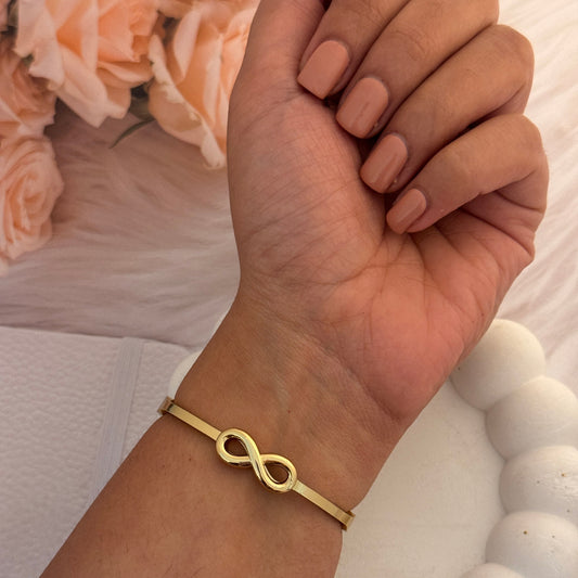 Gold bracelet with infinity symbol on wrist, soft background with flowers