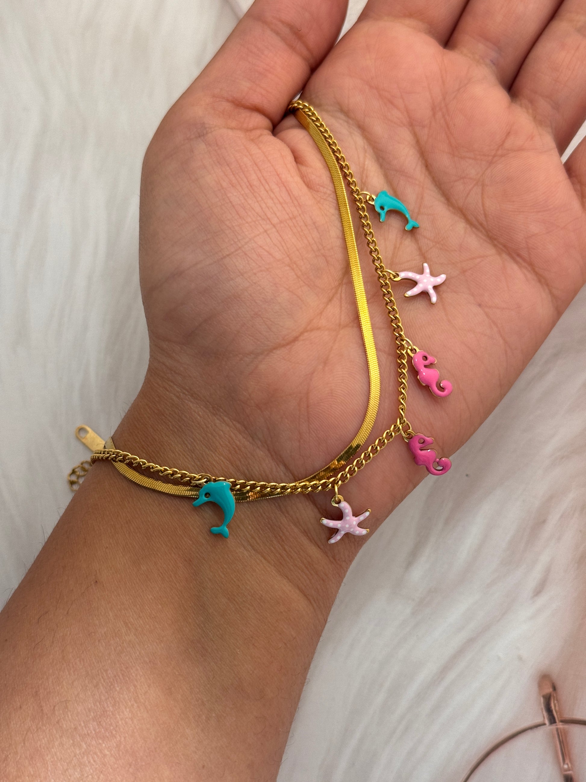 Gold bracelet with colorful starfish charms on a wrist against a white background