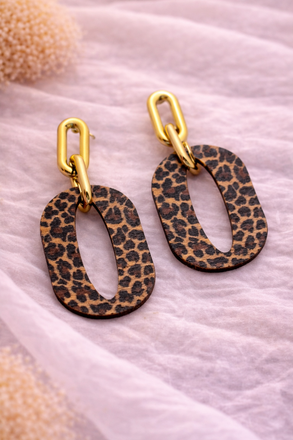 Leopard print earrings with gold hooks on a textured pink surface