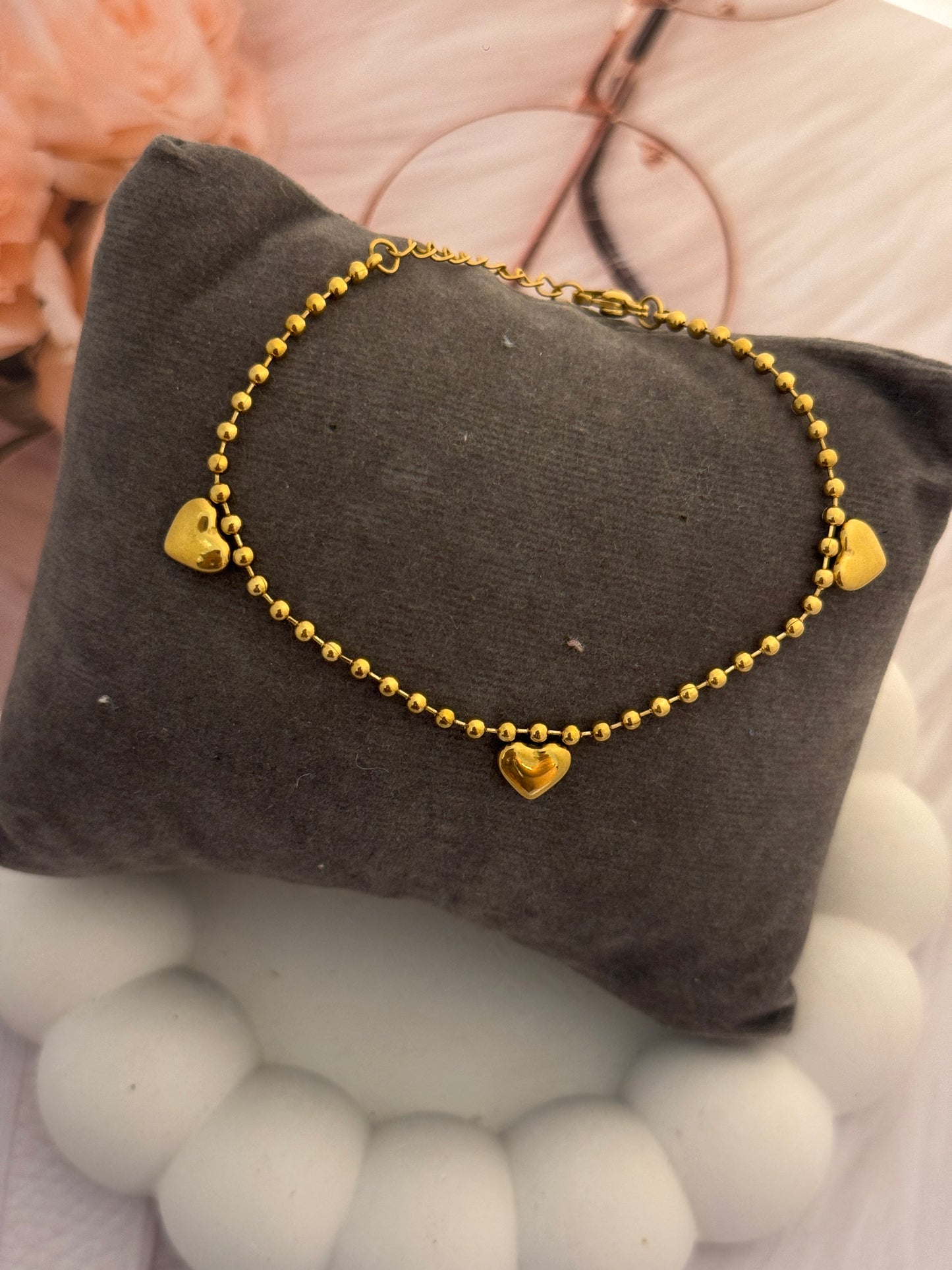 Gold bracelet with heart charms on a gray pillow