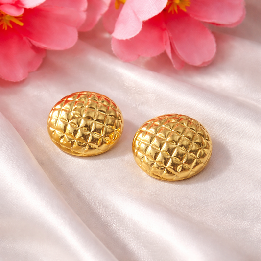 Gold textured earrings on a white fabric background with pink flowers.